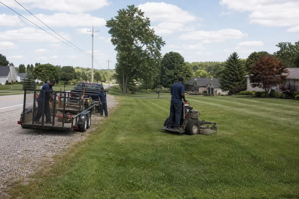 Zero-turn mower cutting a long roadside lawn on a wide lot