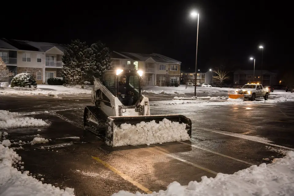 Skid steer clearing apartment complex parking stalls at night