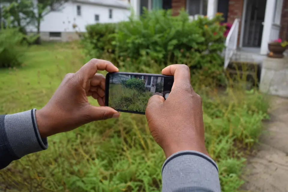 Homeowner taking a phone photo of an overgrown front bed