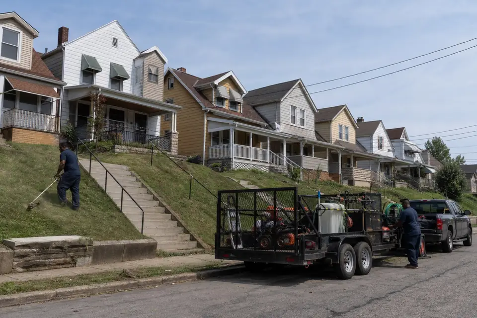 Worker trimming a steep front bank on a sloped street of older homes