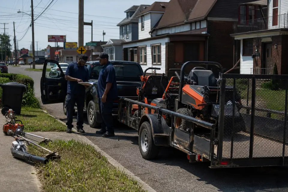 Two crew members talking beside their truck and mower trailer