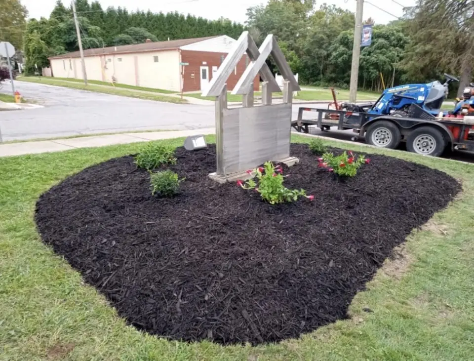 New mulch bed with flowers around a sign, with the mower trailer parked behind