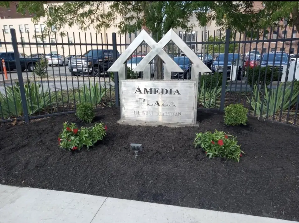 Fresh black mulch bed with red flowers and shrubs around an apartment building sign